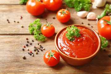 Bowl with sauce, tomatoes, greenery and spices on wooden table