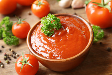 Bowl with sauce, tomatoes, greenery and spices on wooden table