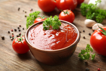 Bowl with sauce, tomatoes, greenery and spices on wooden table