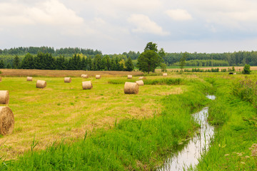 Countryside landscape with hay bales on harvested grain field and stream © irena iris szewczyk