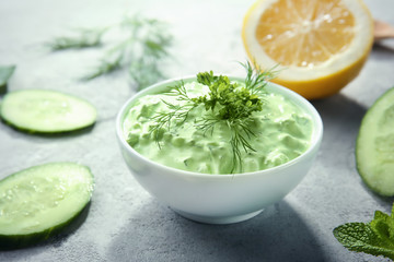 Delicious yogurt sauce in bowl with ingredients on kitchen table