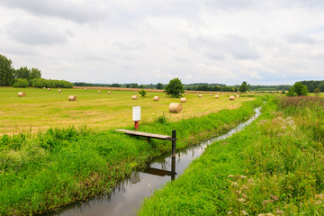 Countryside landscape with hay bales on harvested grain field and stream