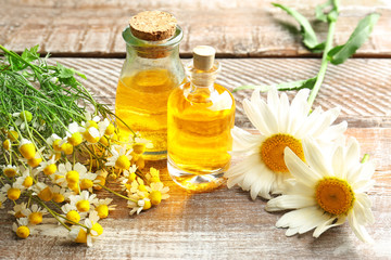 Bottles of essential oil and chamomile flowers on table