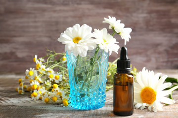 Bottle of essential oil and chamomile flowers on table