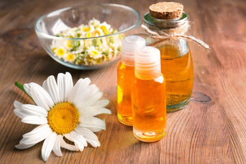 Obraz na płótnie Canvas Bottles of essential oil and chamomile flowers on table