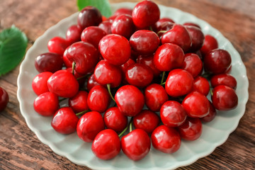 Plate with fresh ripe cherries on wooden background
