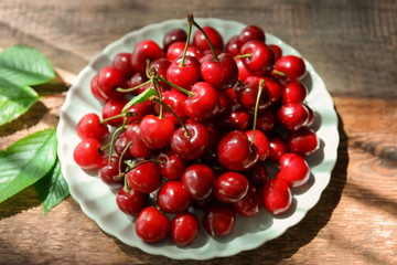 Plate with fresh ripe cherries on wooden background
