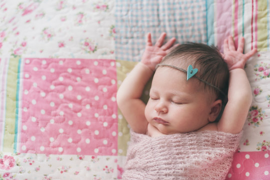 Newborn baby girl sleeping on a patchwork blanket