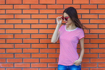 Portrait of beautiful young girl in red sunglasses over red brick wall background