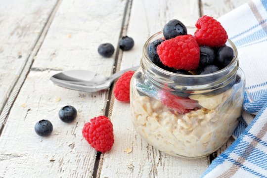 Overnight oats with fresh blueberries and raspberries in a jar on a rustic white wood background