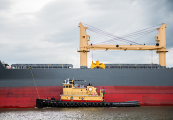 Tugboat guides an industrial tanker through a waterway