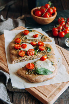 Pizza with pesto, mozzarella and cherry tomatoes on chopping board