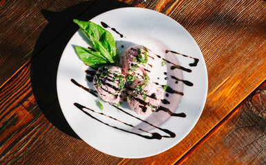 three scoops of pink ice cream in bowl with basil and drizzle on top