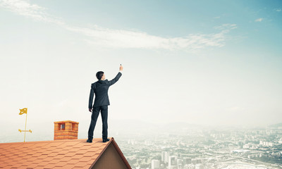 Businessman on house roof touch empty space. Mixed media