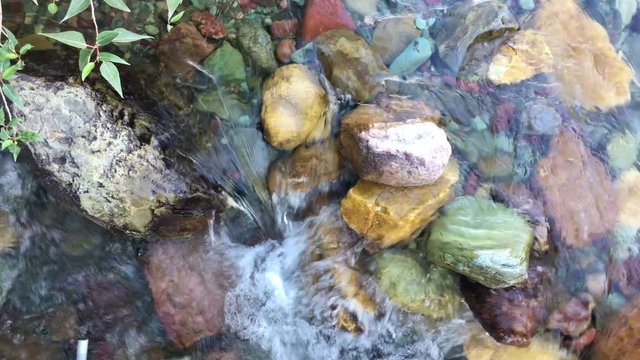 Serene clear water running gently over colorful river rocks
