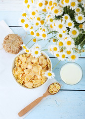 Cornflakes in bowl with glass of milk and chamomile on blue wooden table