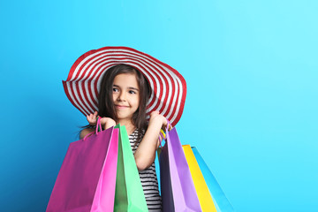 Beautiful little girl with hat and shopping bags on blue background