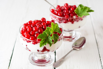 Yogurt dessert with red currant and decorated with leaves on white wooden background
