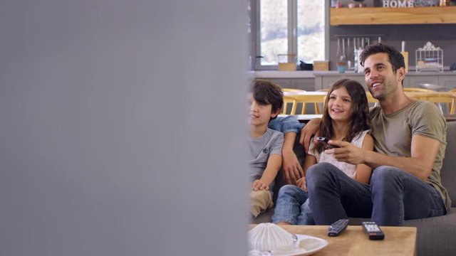 Family Sitting On Sofa In Open Plan Lounge Watching Television