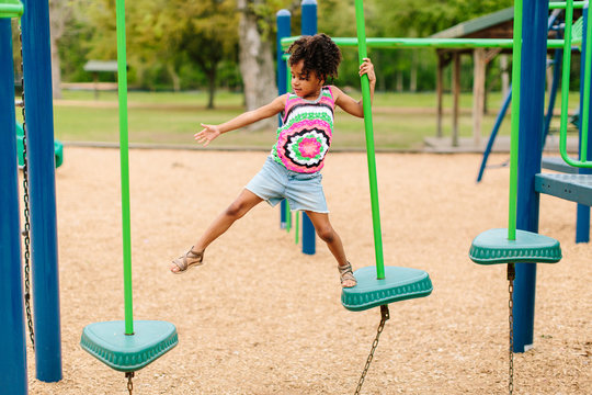 A little girl walking across an obstacle course at the local park.