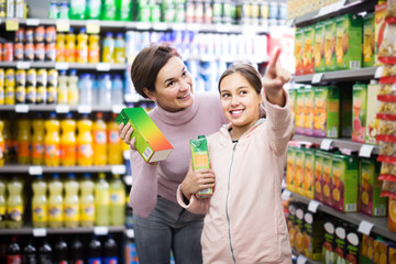 positive woman with daughter choosing refreshing beverages in supermarket
