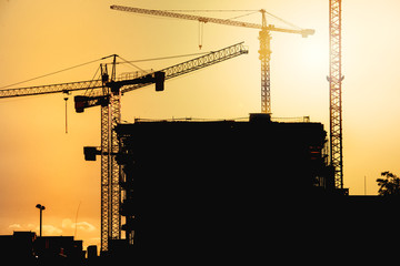 industrial construction site at sunset with silhouettes of tower cranes