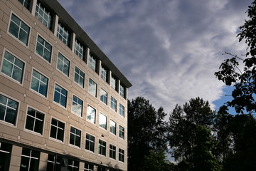 Obraz premium Cloudy sky with illuminated reflected glass facade on modern office building