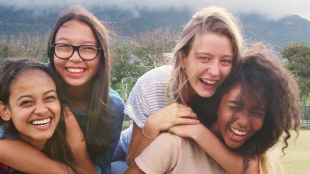 Four happy teenage girls piggybacking outdoors, close up