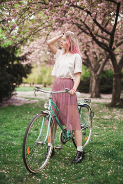 Girl with a pink hair with the bike in the blossoming park