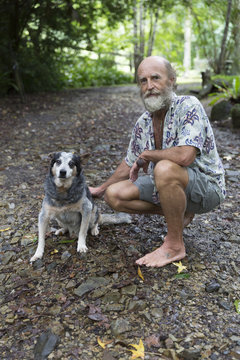 Senior alternative lifestyle male squatting and patting old dog