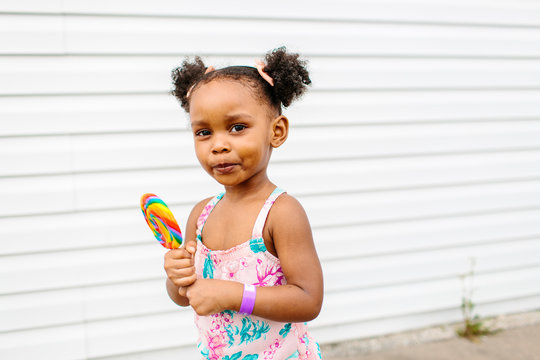 A happy girl with pigtails and a rainbow colored lollipop