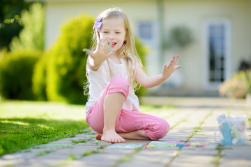 Cute little girl drawing with colorful chalks on a sidewalk. Summer activity for small kids. © MNStudio