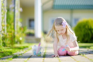 Cute little girl drawing with colorful chalks on a sidewalk. Summer activity for small kids.