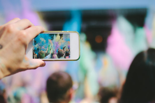 hand with smartphone taking picture of powder throwing crowd at a music festival
