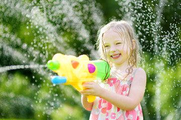Adorable little girl playing with water gun on hot summer day. Cute child having fun with water...
