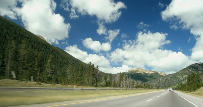 Point of View moving driving down mountain highway with pine trees, some killed by pine beetle, on spring summer day on I-70 Rocky mountains Colorado 4K