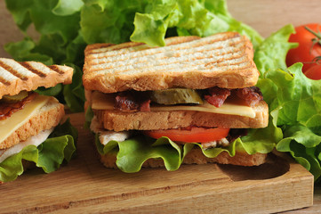 multilayered sandwich with cheese, bacon, chicken, tomatoes, pickles