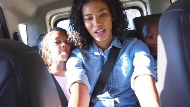 Young black mother taking photos with two children in a car