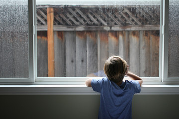 Boy looks out window on a rainy day