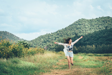 Fototapeta premium Happy young Asian woman running with arm raising outdoor to enjoy the nature with mountain in background