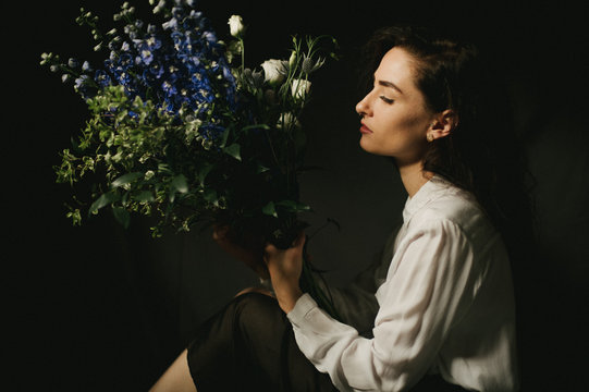 Model with white button up shirt, purple flower bouquet in basement lit by natural window light