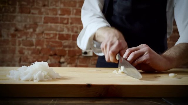 Cookery lessons. The chef cutting one clove of garlic on wooden chopping board for preparing food. 4K