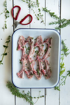 Lamb chops with rosemary and thyme in a baking dish on white wooden background