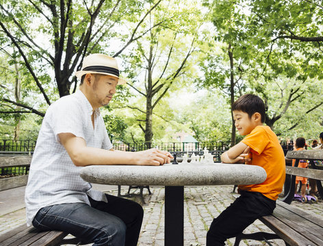Asian father and son, playing chess at park in summer