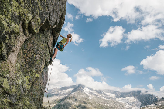 young sporty blonde female rock climber climbing an overhang in high alpine terrain