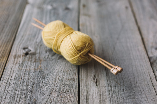 Yellow ball of wool with bamboo needles on rustic wood table