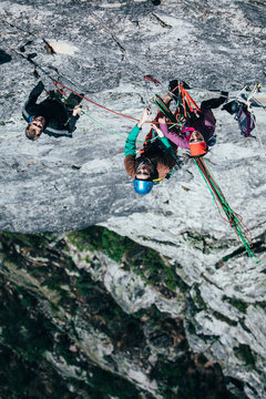 team of climbers hanging from a belay stance on a mountain cliff