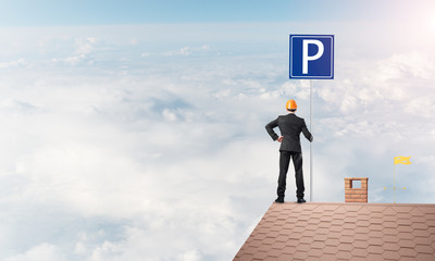 Young businessman with parking sign standing on brick roof. Mixed media