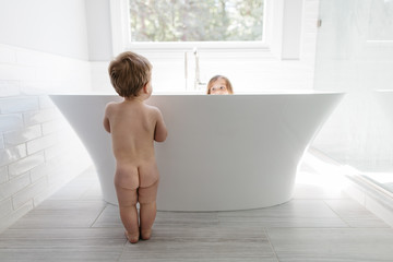 Naked toddler looking at her sister in a big bathtub