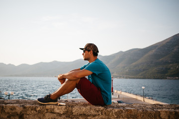 Young man sitting at a wall smoking a cigarette